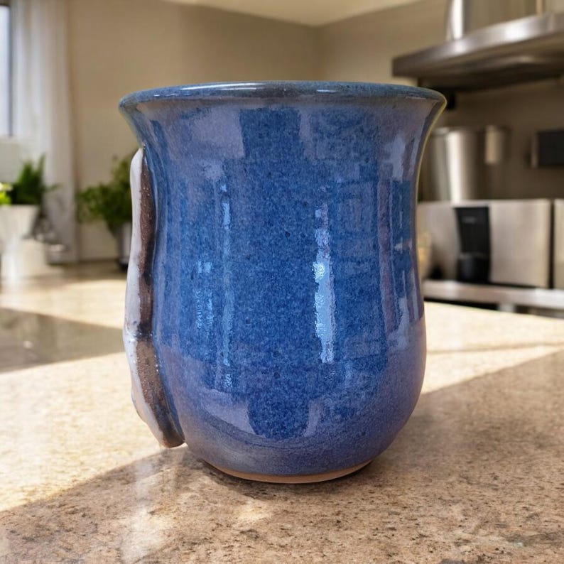 May include: A blue ceramic mug with a white and brown glaze. The mug has a unique, slightly asymmetrical shape.