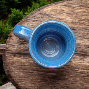 K&ouml;nnte beinhalten: Eine blaue Keramiktasse mit Henkel. Die Tasse ist leer und hat eine glasierte Oberfl&auml;che.