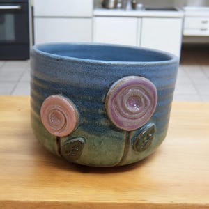 May include: A blue ceramic bowl with a green glaze and two pink and purple flowers with swirl designs.
