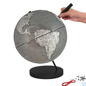 May include: A gray and white globe with a black base and stand. The globe is being marked with a black pen. The globe has a detailed map of the world. Includes pins and red string.