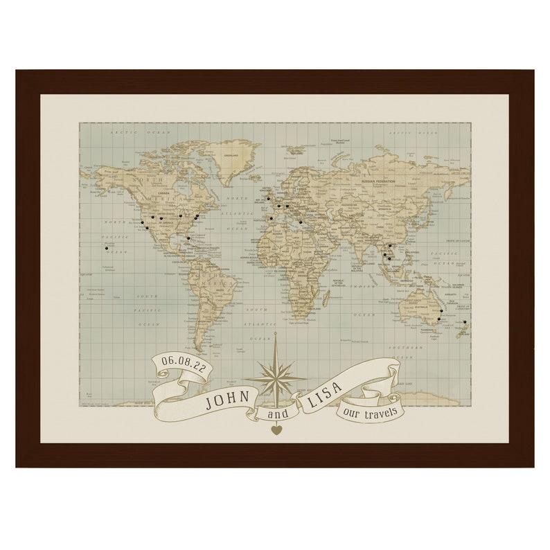 May include: A vintage-style world map with push pins marking locations. The map is framed in a brown frame and has a banner at the bottom that reads "06.08.22 John and Lisa our travels".