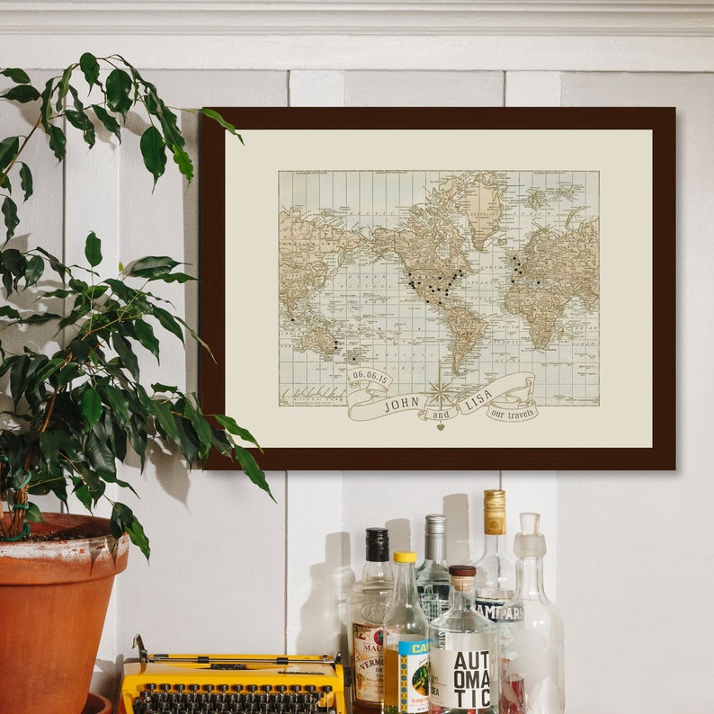 May include: A framed world map with push pins marking locations. The map is in a brown frame and has a cream background. The text "John and Lisa, our travels" is printed below the map.