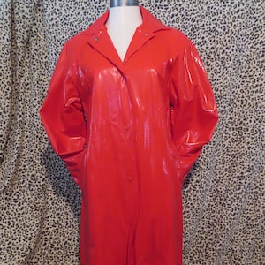 Puede incluir: Una gabardina larga de color rojo con cierre de botones y cuello. La gabardina está hecha de un material brillante e impermeable.