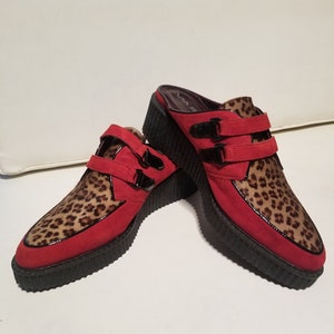 May include: Red and leopard print platform shoes with buckle straps. The shoes have a chunky platform sole and a pointed toe.