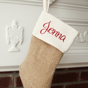 May include: A burlap Christmas stocking with a white cuff and the name "Jenna" embroidered in red.
