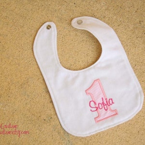 May include: White bib with pink embroidered number one and the name Sofia.