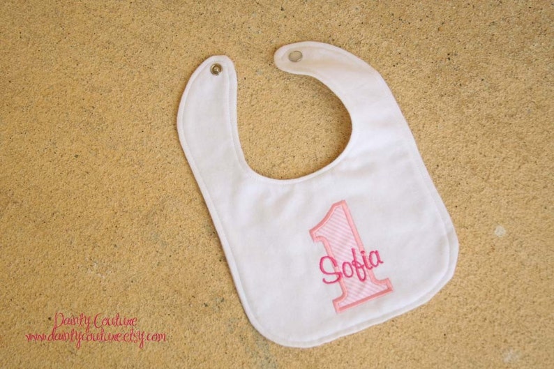 May include: White bib with pink embroidered number one and the name Sofia.