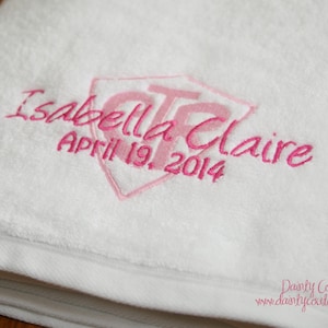 May include: White towel with pink embroidery. The embroidery includes the name "Isabella Claire" and the date "April 19, 2014".