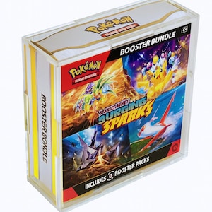 May include: A clear acrylic box containing a Pokémon TCG Booster Bundle. The box features colorful artwork from the "Scarlet & Violet - Surging Sparks" expansion, including Pikachu and other Pokémon characters. The bundle includes booster packs.