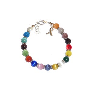 May include: A multi-colored beaded bracelet featuring round cat's eye beads in various hues including blue, green, red, yellow, and purple. The bracelet includes small silver-toned metal spacers between the beads and a metal awareness ribbon charm.
