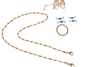 May include: A gold-toned metal eyeglass chain featuring alternating small round beads and elongated oval links, paired with a pair of rimless scalloped-edge sunglasses, four light blue silicone eyeglass connectors, and a single gold-toned ring.