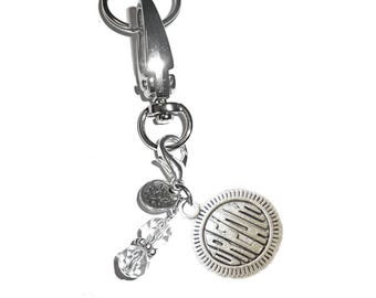 May include: A silver-toned metal keychain featuring a large lobster clasp, a circular charm embossed with the word DREAM, a smaller circular charm with a lotus flower design, and two clear, faceted glass beads separated by small silver spacers.