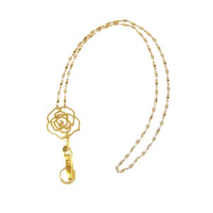 May include: A gold-toned lanyard featuring a delicate, open-work rose pendant attached to a metal lobster clasp. The chain consists of small, elongated, textured links that create a continuous loop, providing a functional and decorative accessory.