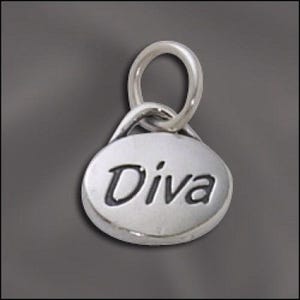 May include: A small, oval-shaped silver charm featuring the word Diva engraved in black lettering on the front surface. The charm includes a circular jump ring attached to the top, allowing it to be easily suspended from a chain or bracelet.