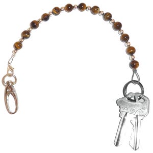 May include: A brown tiger's eye beaded keychain with a silver clasp and two silver keys. The keys have the text "SCI 66" on them.