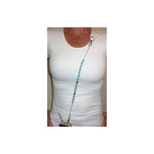 May include: A phone lanyard featuring a series of round turquoise beads and small silver-toned metallic spacers strung on a thin silver-colored chain. The accessory includes silver-toned lobster claw clasps at both ends for attachment to a mobile device.