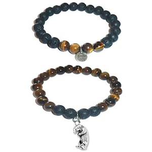 May include: Two beaded bracelets. The top bracelet features black porous lava beads and brown tiger eye beads with a silver lotus flower charm. The bottom bracelet consists of brown tiger eye beads and black lava beads with a silver otter charm.