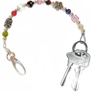 May include: A beaded keychain featuring a variety of colorful glass, stone, and silver-toned metal beads arranged in a strand. The strand includes a silver-toned lobster clasp on one end and a metal split ring holding two silver-toned keys on the other.