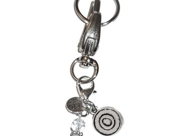 May include: A silver-toned metal keychain featuring a large lobster clasp and a split ring. Attached to the swivel connector are two small circular charms, one with a lotus flower design and one with a concentric circle pattern, plus two clear beads.