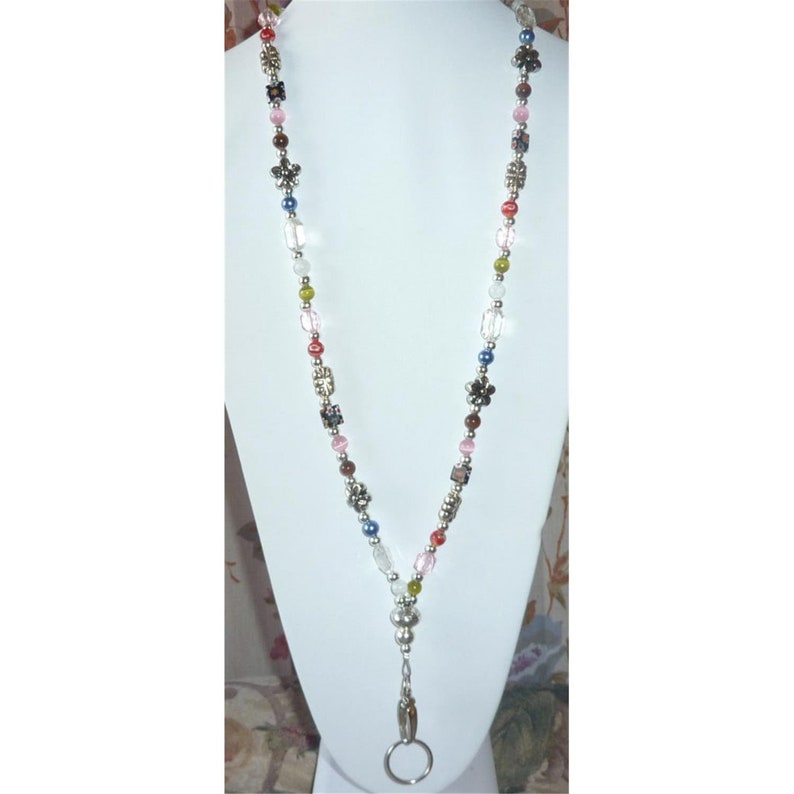 May include: A beaded lanyard with a silver retractable badge holder. The lanyard features a variety of colorful beads, including clear, pink, red, green, brown, and blue.
