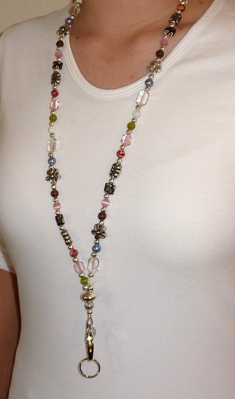 May include: A colorful beaded lanyard with a silver clasp and a silver ring at the end. The beads are various shades of pink, red, green, blue, and brown.
