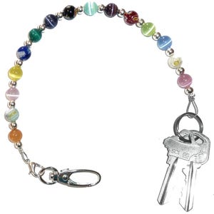 May include: A beaded keychain featuring a variety of colorful, round, cat's eye style beads interspersed with small silver-toned metal spacer beads. The strand is attached to a silver-toned lobster clasp on one end and a metal key ring with two keys.
