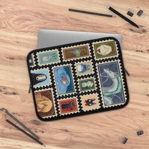Puede incluir: Una funda rectangular para portátil con fondo negro y un patrón repetitivo de ilustraciones estilo sello postal. Los sellos representan varios personajes animados, incluyendo un dragón blanco, un gato negro y una figura enmascarada, en colores.
