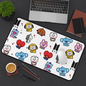 May include: A rectangular white desk mat featuring a repeating pattern of colorful BT21 cartoon characters, including Tata, Chimmy, Cooky, Koya, RJ, Shooky, Mang, and Van, interspersed with small red hearts and the black BTS logo text.