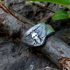 May include: A silver ring with a skull and moth design. The ring is handcrafted by Doctor Gus Original.