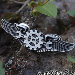 May include: A silver metal pin with a gear and wings. The pin is handcrafted and says "Doctor Gus Original" on the bottom.