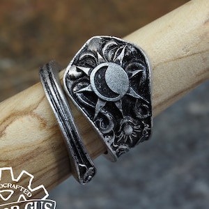 May include: A silver ring with a sun and moon design. The ring is handcrafted and features intricate details. The ring is on a wooden surface.