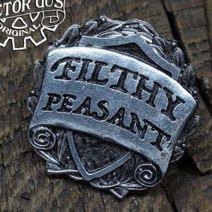 May include: A silver-toned metal pin with a scroll design and the words "Filthy Peasant" in black lettering. The pin is surrounded by a decorative leaf design.