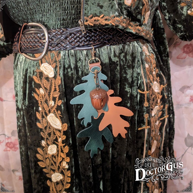 May include: A green velvet dress with gold embroidery and a brown leather belt. A green and brown leather acorn charm hangs from the belt.