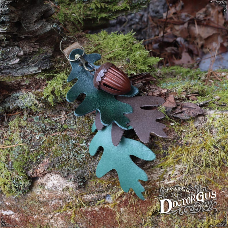 May include: A leather acorn charm with a green and brown oak leaf design. The charm is attached to a key ring. Handcrafted by Doctor Gus Original.