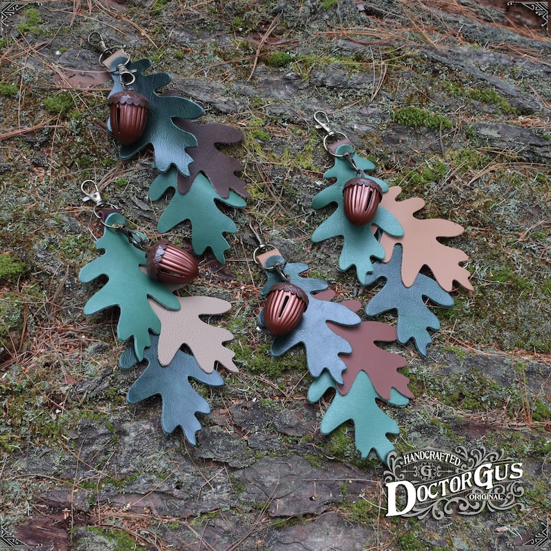 May include: Four leather acorn charms with oak leaf designs in shades of green, brown, and tan. Each charm features a small, detailed acorn with a metal loop for attaching to a keychain or bag.