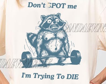 Peut inclure: Un t-shirt blanc avec un graphique d'un raton laveur soulevant des poids. Le texte sur le t-shirt est "Don't SPOT me I'm Trying To DIE."