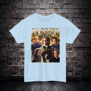 Op de afbeelding: Lichtblauw T-shirt met een grafische print van vier mannen. De grafiek bevat de tekst "Jasper Hale" in gouden letters.