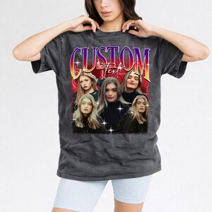 May include: Dark gray t-shirt featuring a graphic design with the word "CUSTOM" in a purple and yellow gradient font. Below the text are five portraits of women with long blonde hair. The background has a red lightning bolt design.