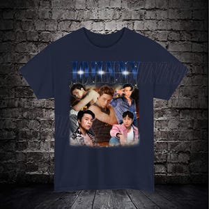May include: A navy blue t-shirt with a vintage-style graphic featuring a collage of five men. The graphic includes the word "JOHNNY" in large, bold letters with a glittery effect.