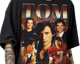 May include: A black short-sleeve t-shirt featuring a graphic print of actor Tom Welling. The design includes the text "TOM" in large metallic letters at the top, "Welling" in script below, and a collage of five different photos of the actor.