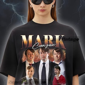 Peut inclure: T-shirt noir avec un imprimé graphique de Mark Corrigan de la série télévisée "The IT Crowd". Le graphique est un collage d'images de Mark Corrigan et d'autres personnages de la série.