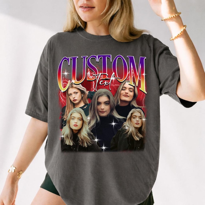 May include: Dark gray t-shirt featuring a graphic with the word "CUSTOM" in a retro font. The graphic includes multiple images of a person with long blonde hair, set against a red and yellow background.