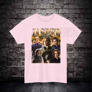 Op de afbeelding: Roze T-shirt met een grafische print van vier mannen. De grafiek bevat de tekst "Jasper Hale" in gouden letters.