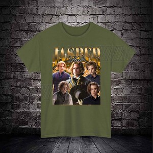 Op de afbeelding: Een groen T-shirt met een grafische print van een groep mensen. De grafiek bevat de tekst "Jasper Hale" in gouden letters.