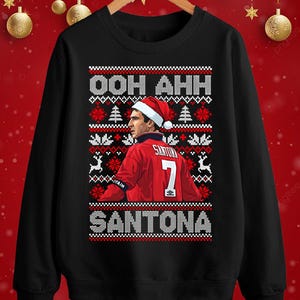 May include: Black sweatshirt with a festive design. The design includes the text "OOH AHH SANTONA" in white, a portrait of a person wearing a Santa hat and a red jersey with the number 7, and Christmas-themed graphics.
