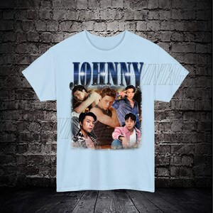 May include: Light blue t-shirt with a vintage-style graphic featuring a group of men with the word "JOHNNY" printed in bold letters.