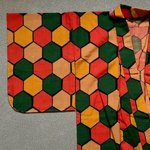 May include: A colorful kimono with a geometric pattern of red, green, yellow, and tan hexagons. The garment is open in the front, with wide sleeves and a collar. The fabric has a slight sheen.