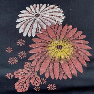 Può includere: Un tessuto blu navy scuro con un disegno ricamato di due grandi fiori di crisantemo, uno bianco e uno rosa polvere con centro giallo, accompagnati da diversi motivi floreali rosa più piccoli e un singolo motivo a foglia rosa dettagliato.