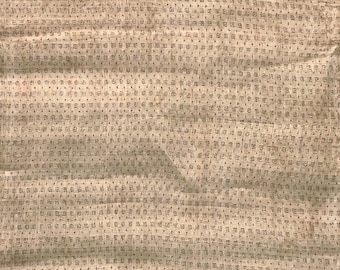 May include: A light tan fabric featuring a repeating grid pattern of small, dark brown, square-shaped symbols. The textile has a visible woven texture with subtle folds and creases across the surface, creating a consistent, uniform geometric design.