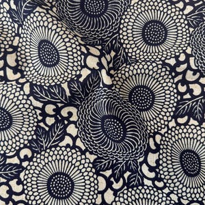 May include: A textile fabric featuring a repeating pattern of dark navy blue chrysanthemum flowers and leaves set against a light beige background. The design consists of dense, circular floral motifs with intricate line work and foliage.